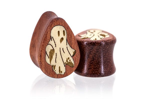 A pair of wooden ear plugs, teardrop shape both featuring an inlayed ghost design.